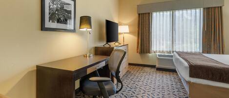 Une chambre d’hôtel équipée d’un bureau, d’une chaise, d’un lit et de grandes fenêtres avec des rideaux.