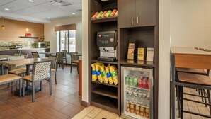 Un restaurante con una máquina de café de servicio propio, un refrigerador lleno de bebidas y zonas de estar con sillas y mesas.