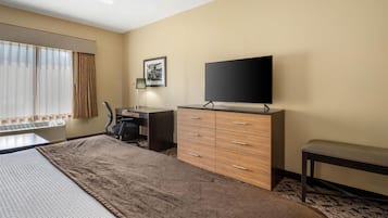 A hotel room with a bed, a desk, a television, and a bench.