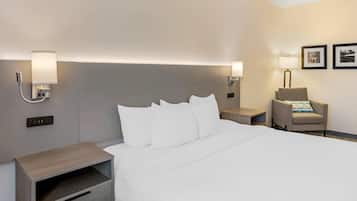 Una habitación de hotel con una cama grande, mesitas de noche, una silla y lámparas de pared.
