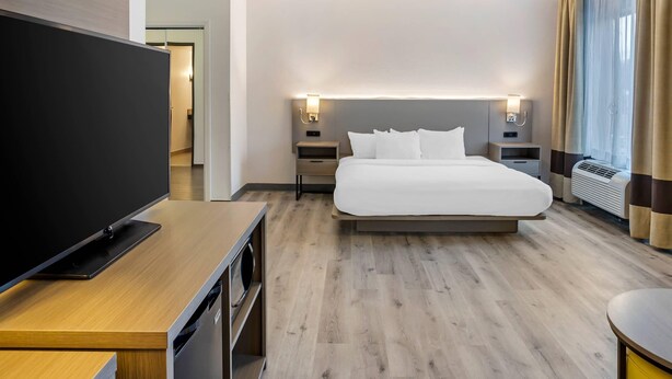 A modern hotel room with a large bed, bedside tables with lamps, a flat-screen TV, and a wooden floor.