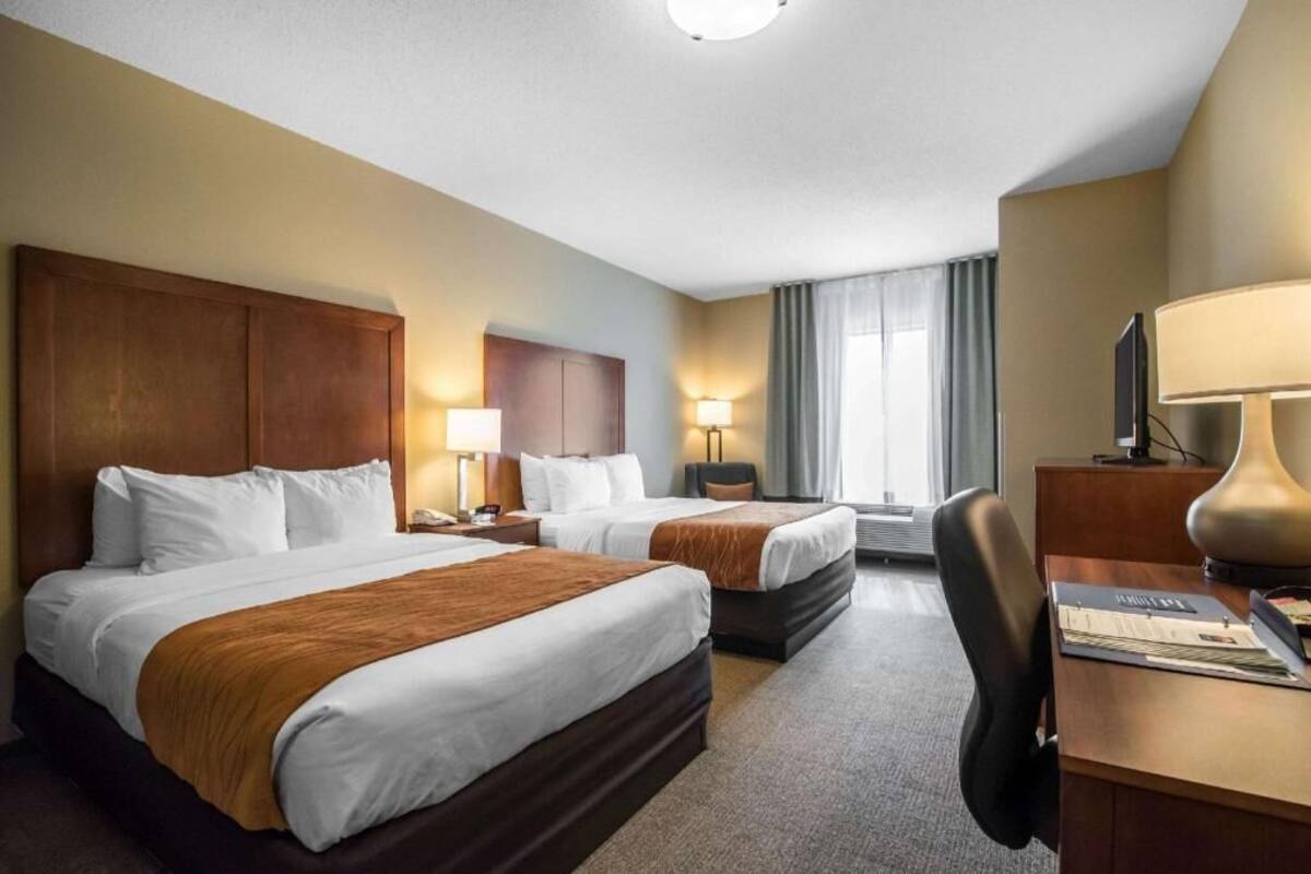 A hotel room with two beds, a desk, a chair, a TV, and a window with curtains.