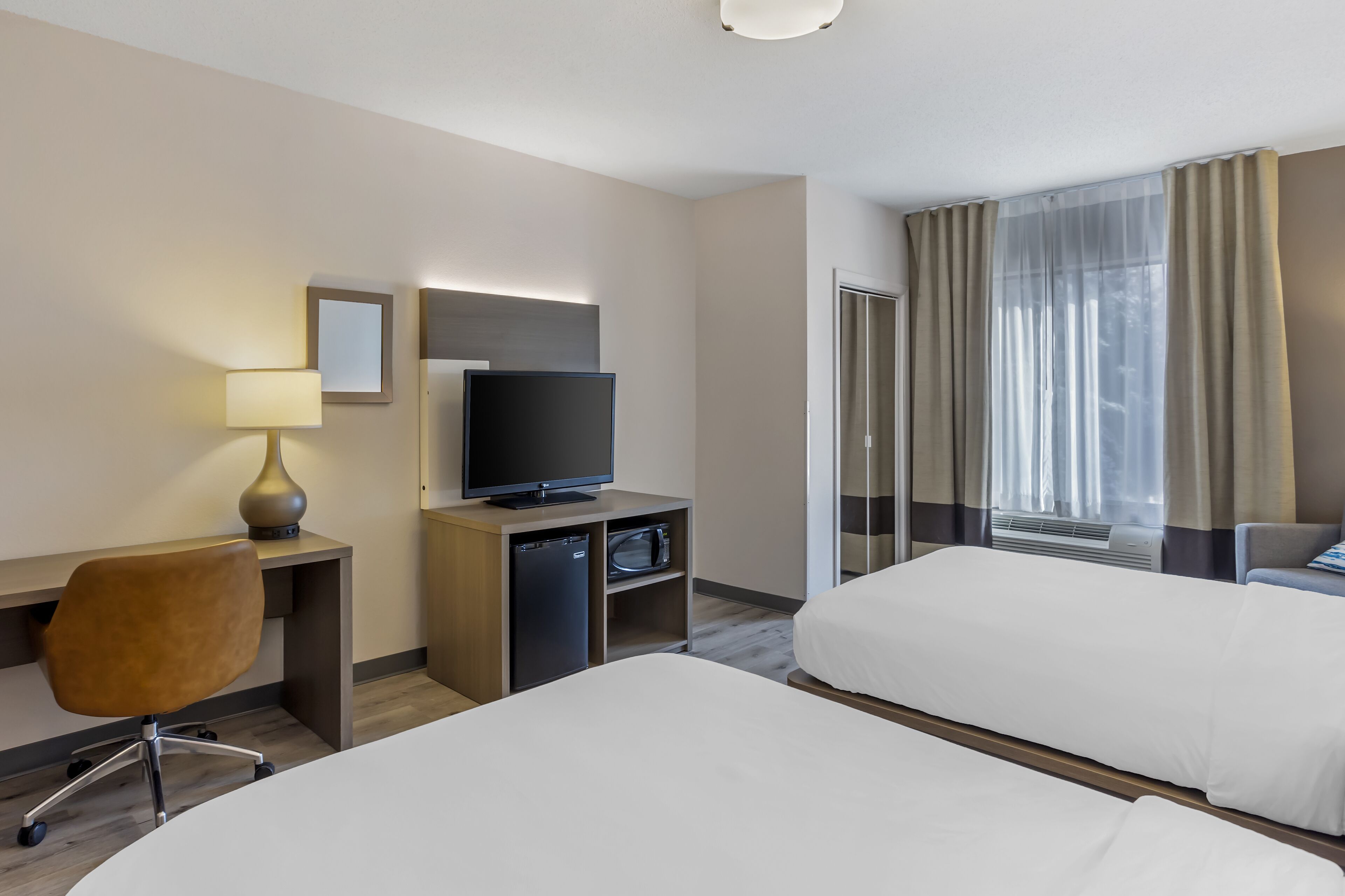 A hotel room with two beds, a desk with a TV, a lamp, and a minibar.