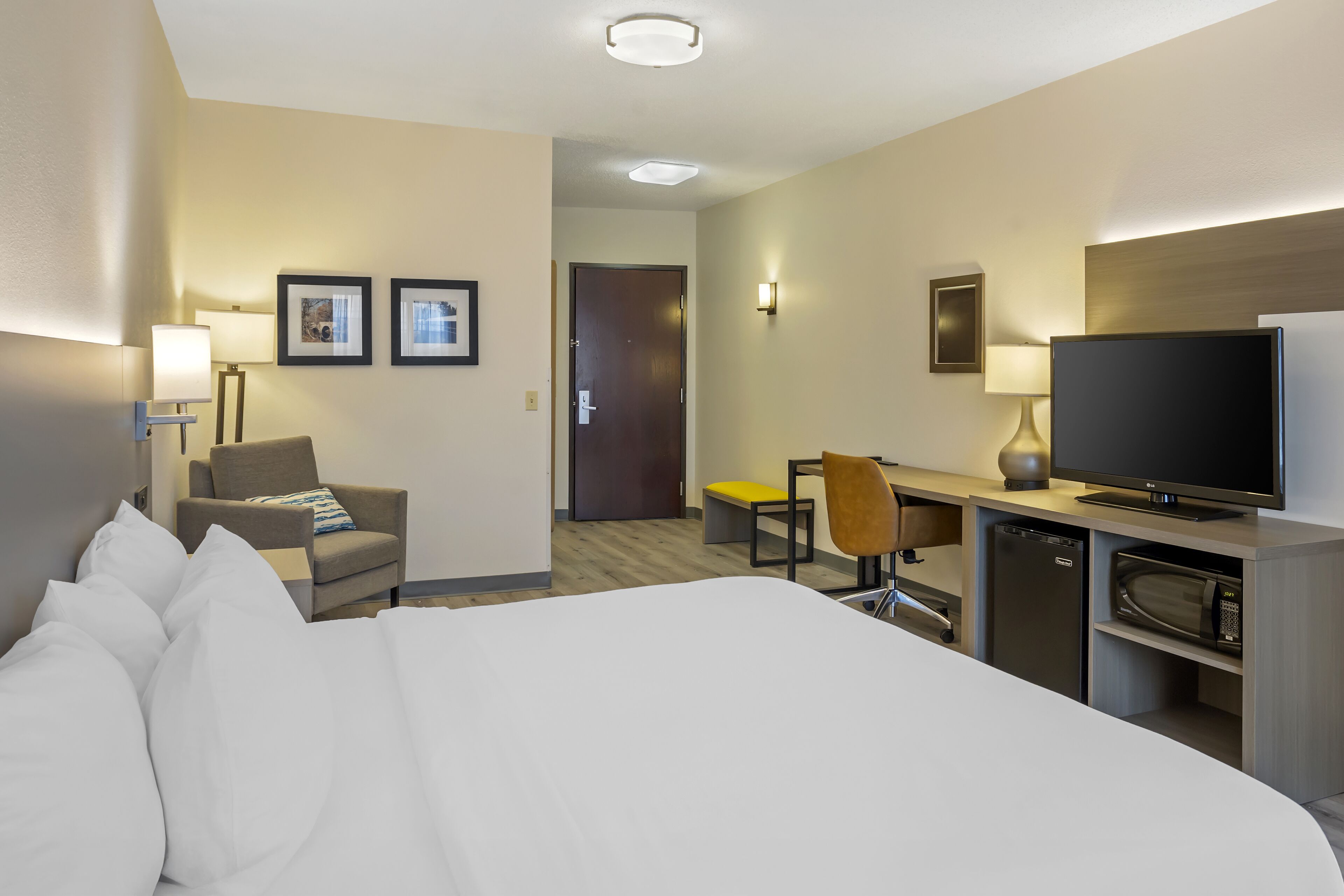 A hotel room with a large bed, a desk with a chair, a television, a microwave, and a door leading to another room.