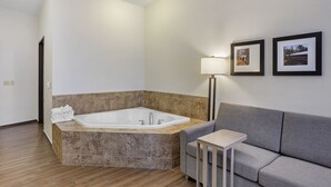 A modern bathroom with a freestanding bathtub, a grey sofa, a small table, and two framed pictures on the wall.