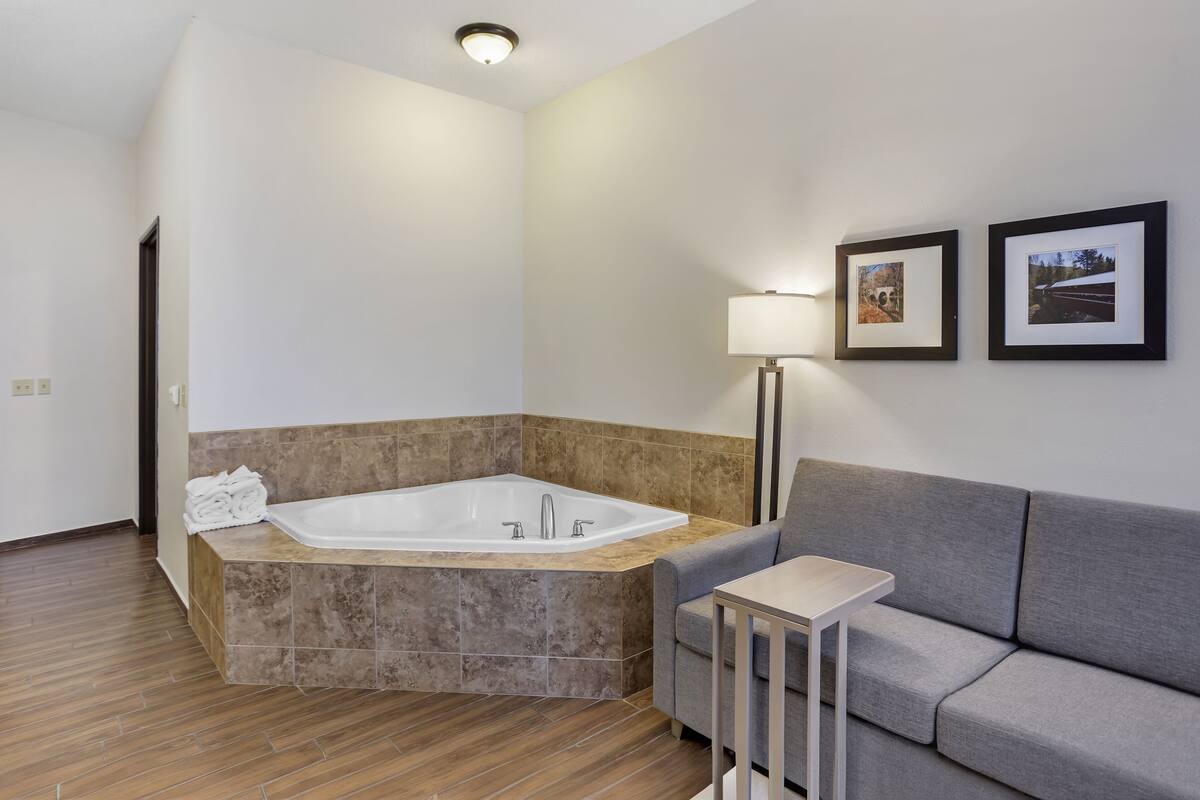 A modern bathroom with a freestanding bathtub, a grey sofa, a small table, and two framed pictures on the wall.