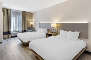 A hotel room with two beds, a desk, a chair, and a window with curtains.