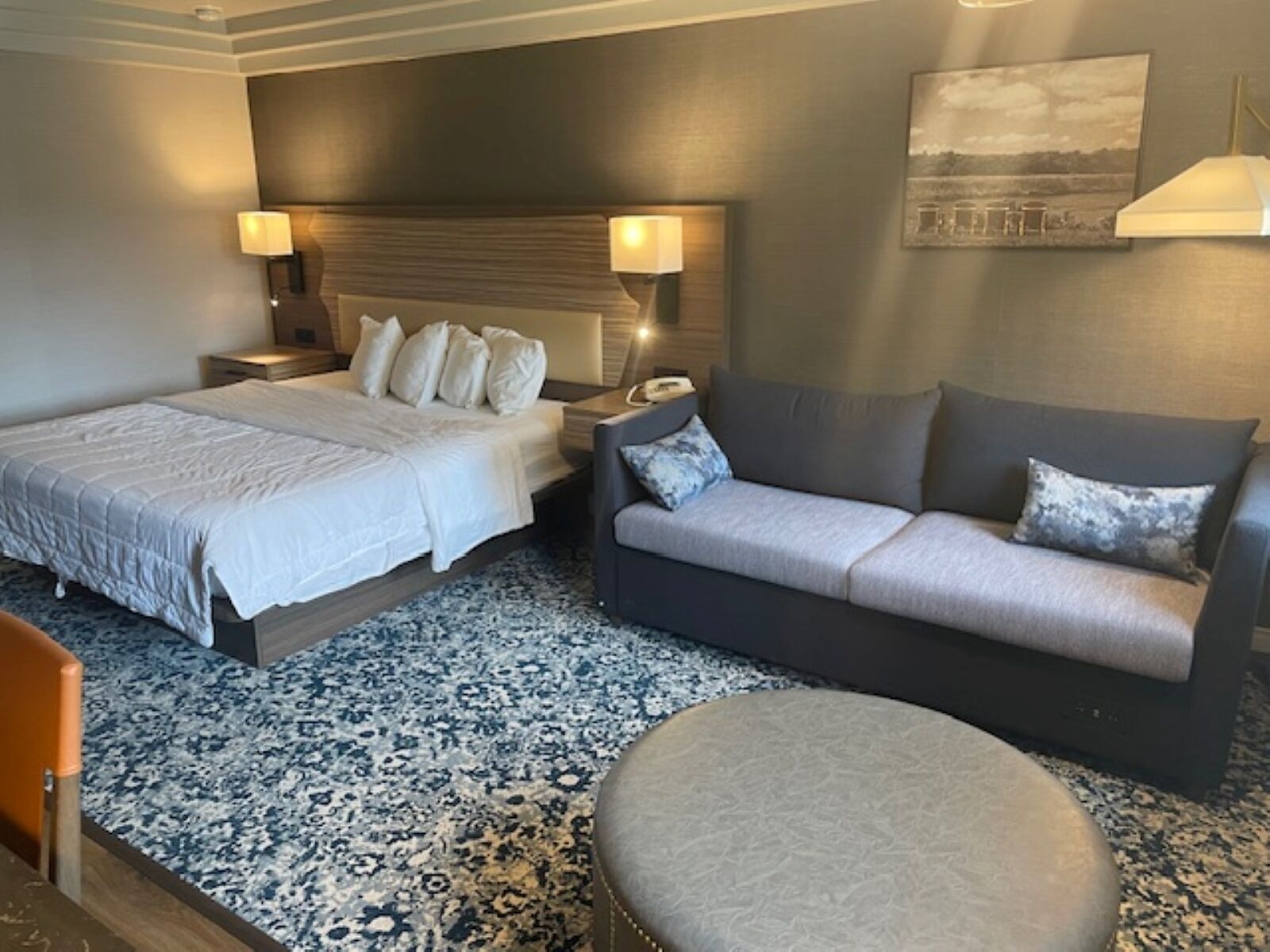 A hotel room with a large bed, a sofa, a small table, and a wall-mounted lamp.
