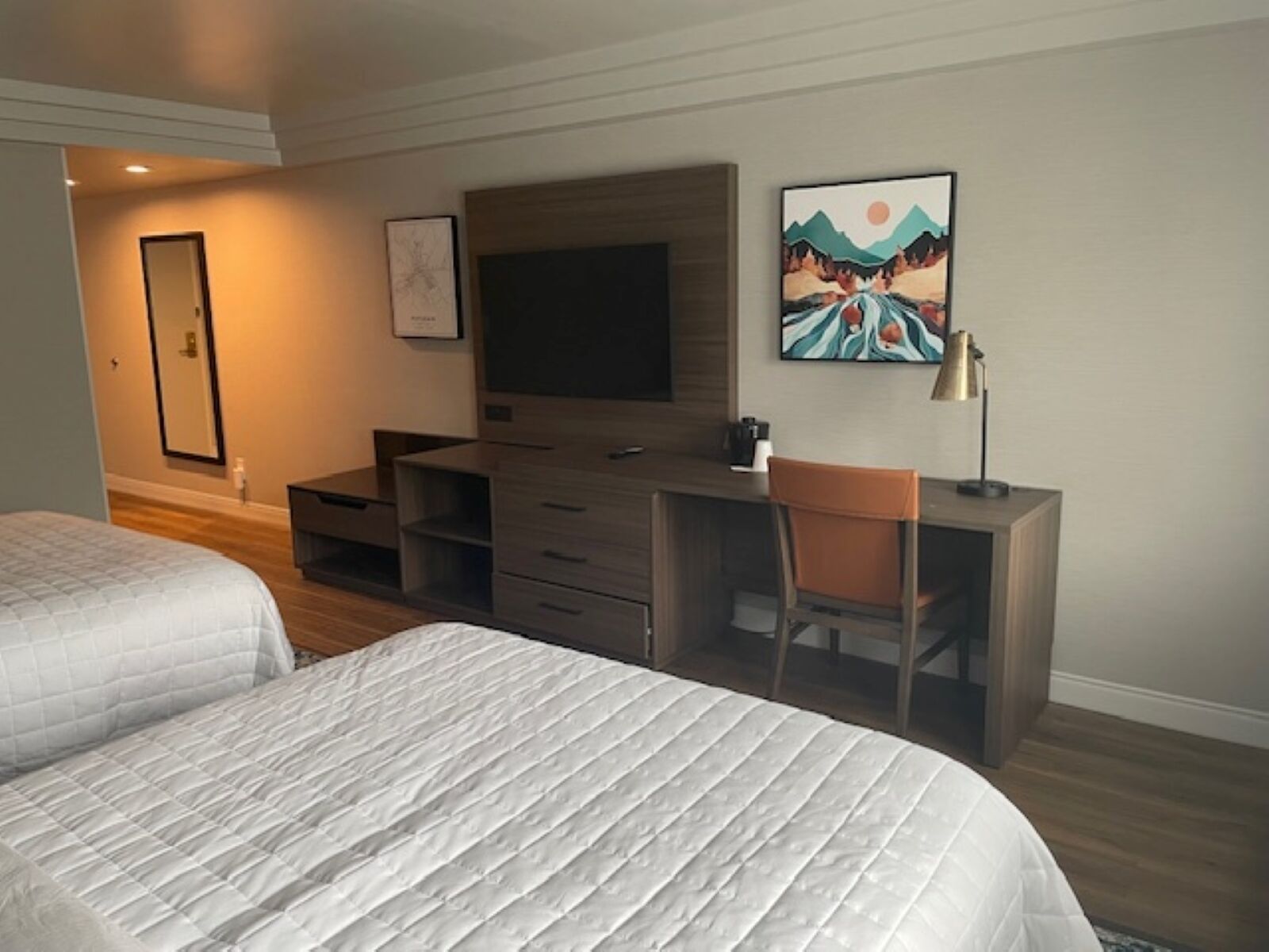 Ein Hotelzimmer mit zwei Betten, einem Schreibtisch, einem Sessel, einem Fernseher und Bildern an der Wand.