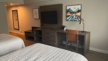 Ein Hotelzimmer mit zwei Betten, einem Schreibtisch, einem Sessel, einem Fernseher und Bildern an der Wand.