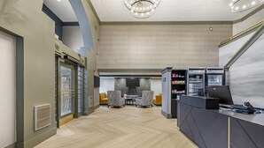 A modern lobby with a herringbone floor, a reception desk, seating area, and a staircase.