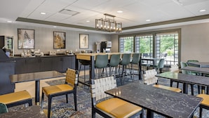 A modern dining area with a bar, multiple seating options, and large windows providing natural light.