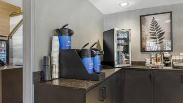 A modern kitchen area with a coffee machine, stacked paper cups, and a refrigerator.