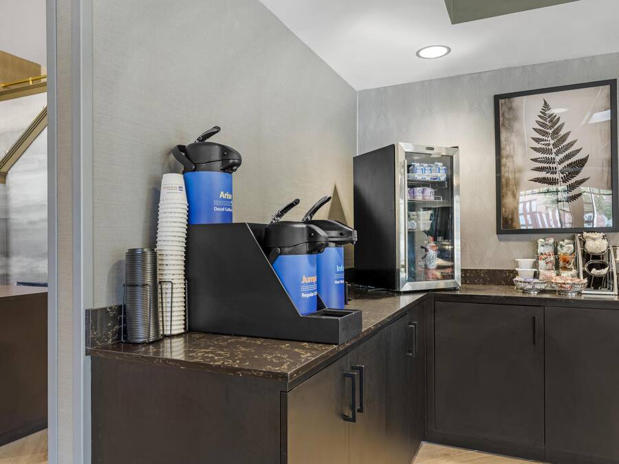 A modern kitchen area with a coffee machine, stacked paper cups, and a refrigerator.
