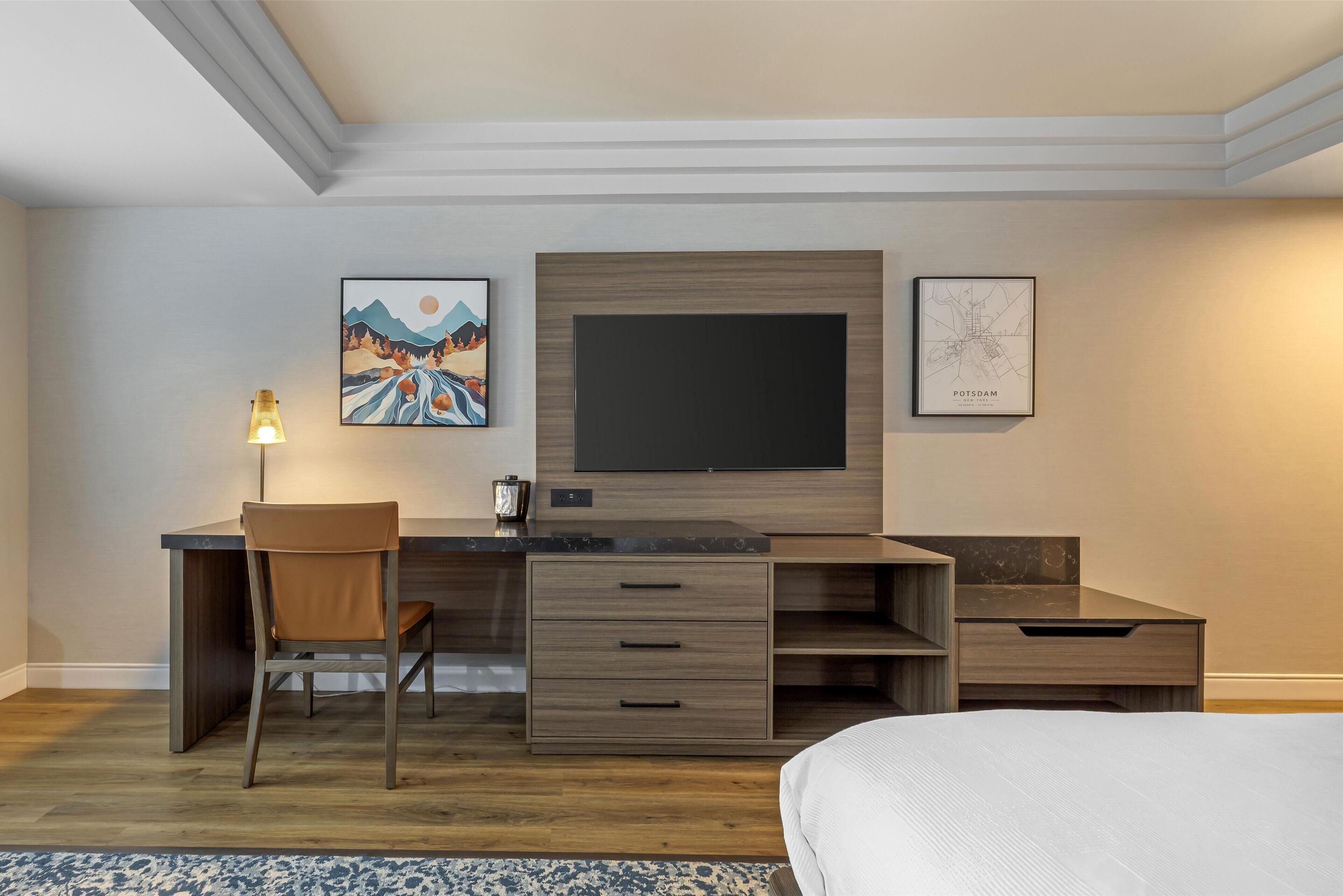 Een moderne slaapkamer met een bed, een bureau met stoel, een flatscreen televisie en kunst aan de muur.