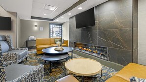 A modern lounge area with patterned sofas, a flat-screen TV, a fireplace, and a patterned carpet.