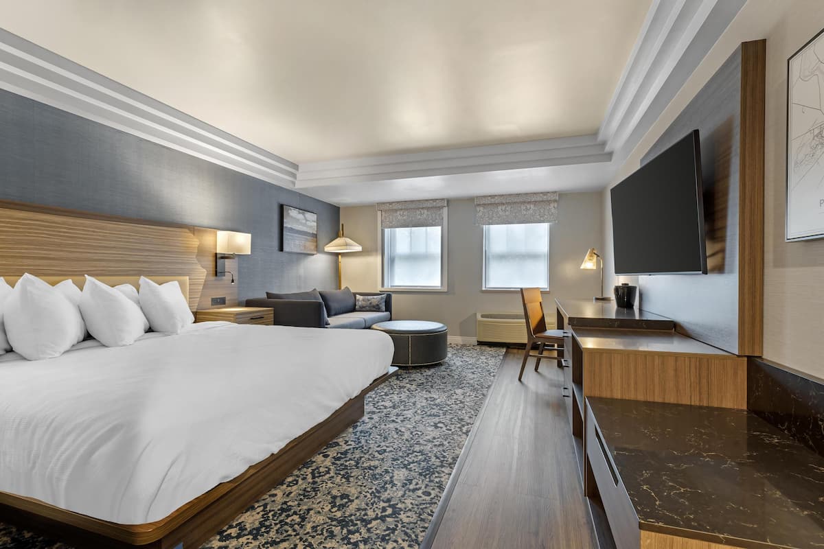 A modern hotel room with a large bed, a sofa, a desk, and a flat-screen TV.