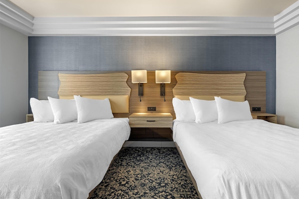 Une chambre d’hôtel avec deux lits, une tête de lit en bois, des lampes de chevet et un tapis à motifs.