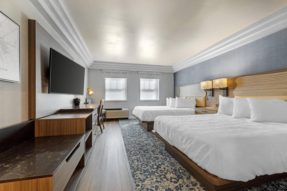 A hotel room with a flat-screen TV, two beds, a desk, and a large window.