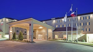 Um hotel com entrada coberta, várias bandeiras e fachada bem iluminada.