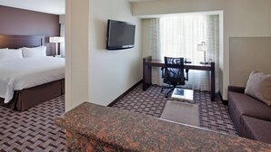 Quarto de hotel com uma cama, uma escrivaninha com cadeira, uma televisão e um sofá.