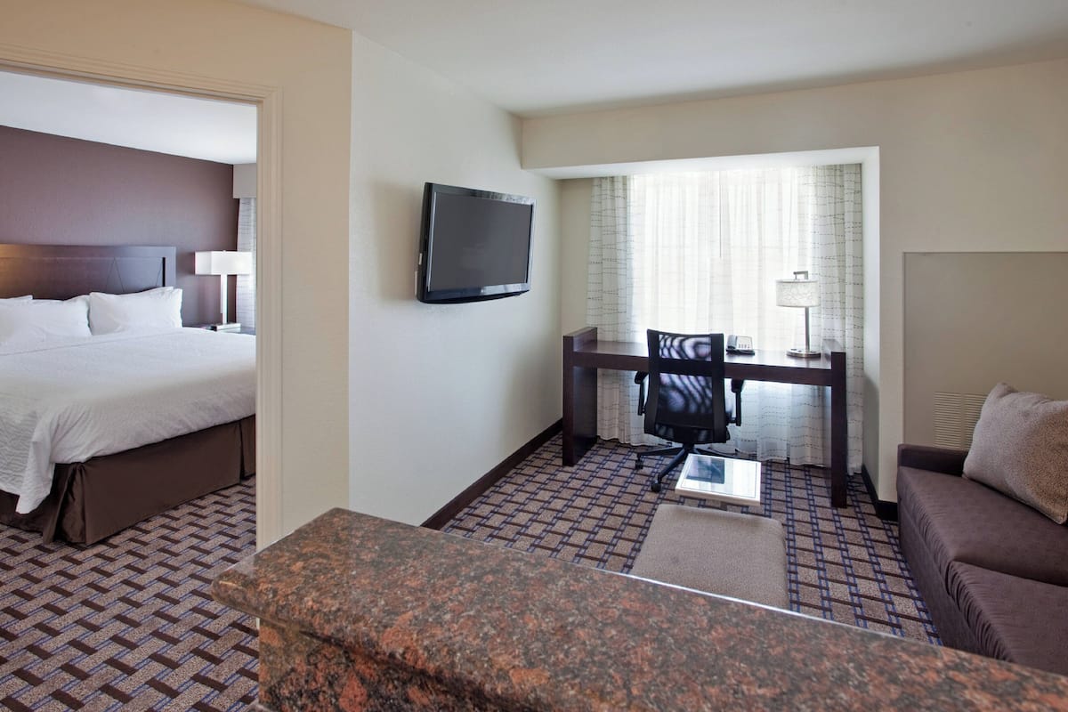 A hotel room with a bed, a desk with a chair, a television, and a sofa.