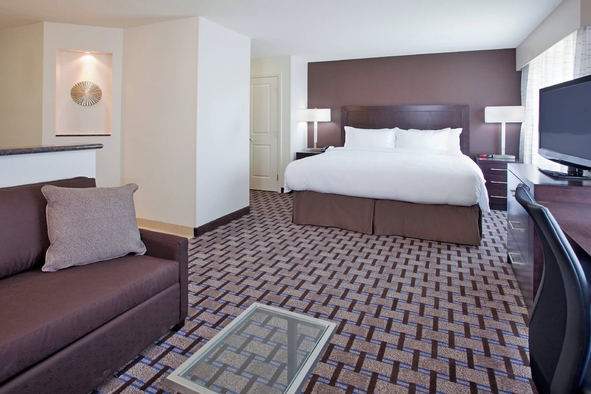 A hotel room with a bed, a sofa, a TV, and a decorative wall piece.