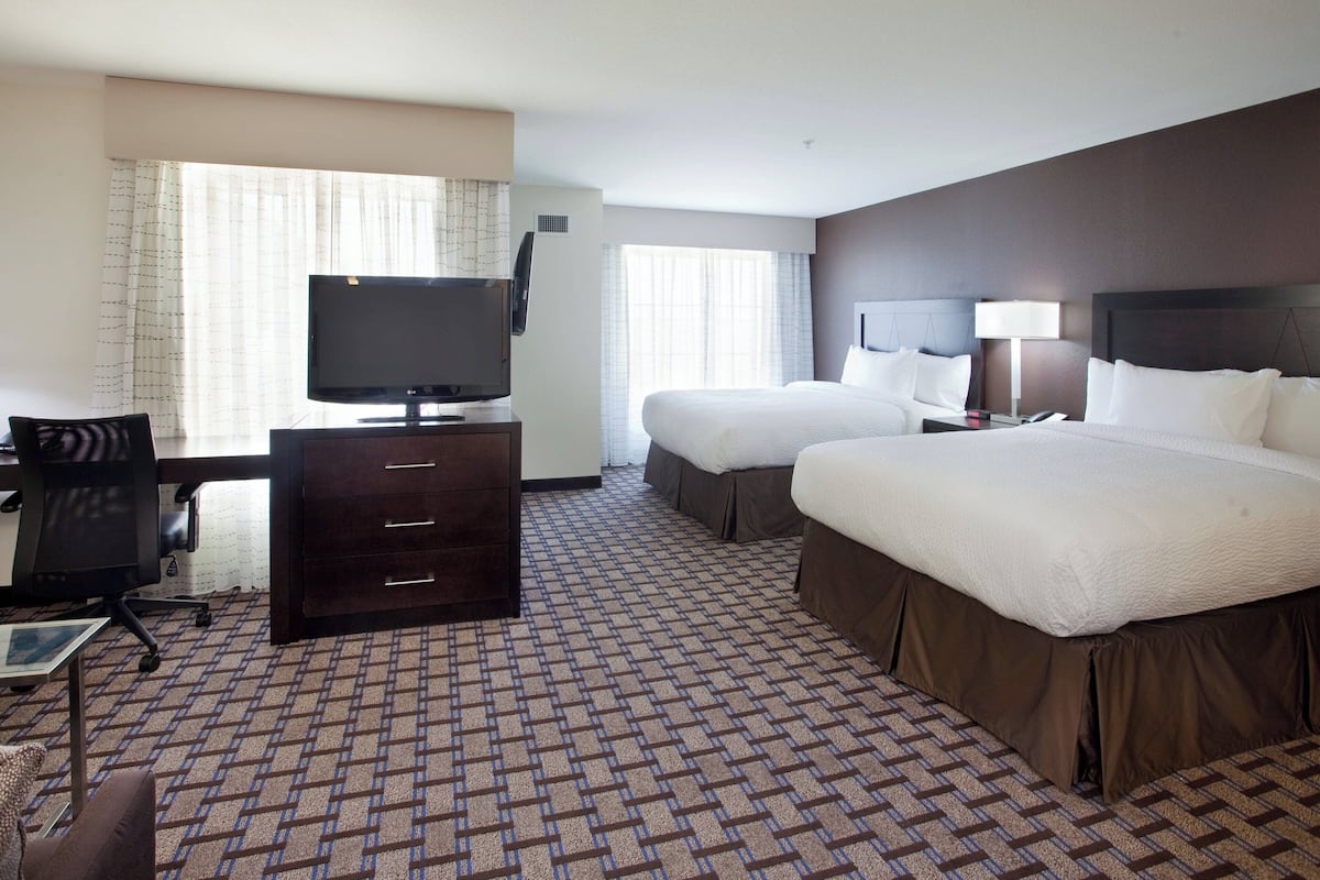 A hotel room with a large bed, a smaller bed, a desk with a computer, a television, and a window with curtains.