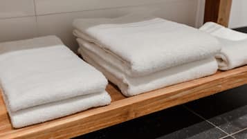 Una pila de toallas blancas sobre un estante de madera en un baño con paredes de azulejos.
