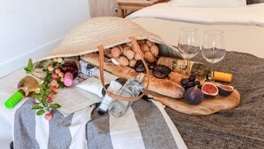 Un plateau de petit-déjeuner avec du pain, des figues, des olives et des verres à vin, disposé sur un lit.