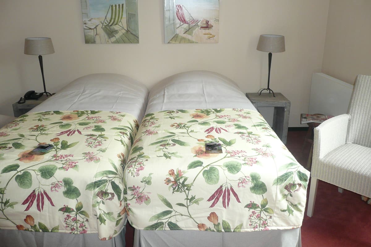 Una cama doble con ropa de cama floral, dos mesitas de noche con lámparas, una silla y dos obras de arte en la pared.