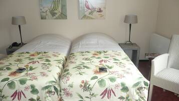A double bed with floral bedding, two bedside tables with lamps, a chair, and two wall art pieces.