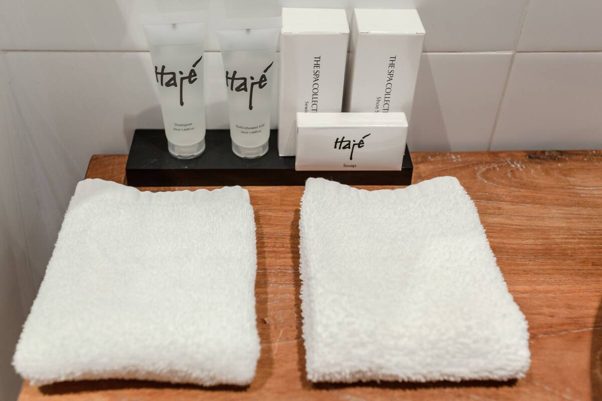 Superficie de madera con dos toallas blancas y una presentación de productos de spa, incluyendo champú, gel de baño y jabón.