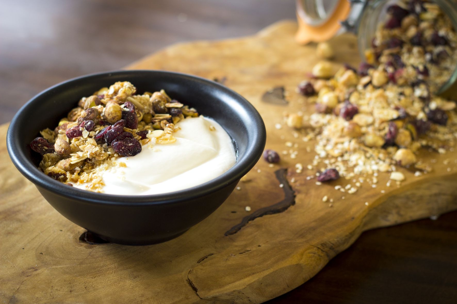 Eine Schale Joghurt mit Granola und Trockenfrüchten auf einem Holzboden.