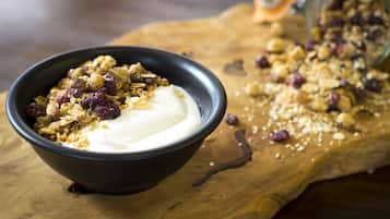 Eine Schale Joghurt mit Granola und Trockenfrüchten auf einem Holzboden.