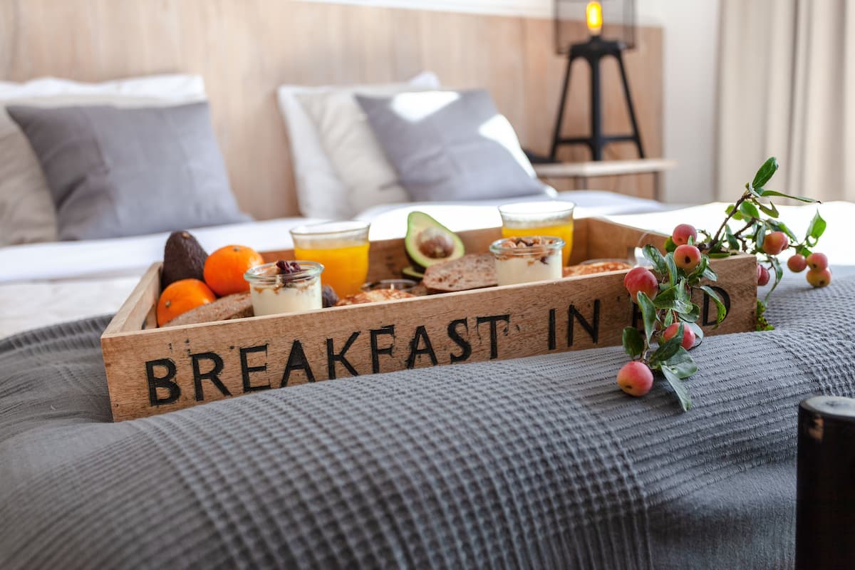 Una bandeja de desayuno con frutas y bebidas sobre una cama, con un cartel que dice 'BREAKFAST IN'.