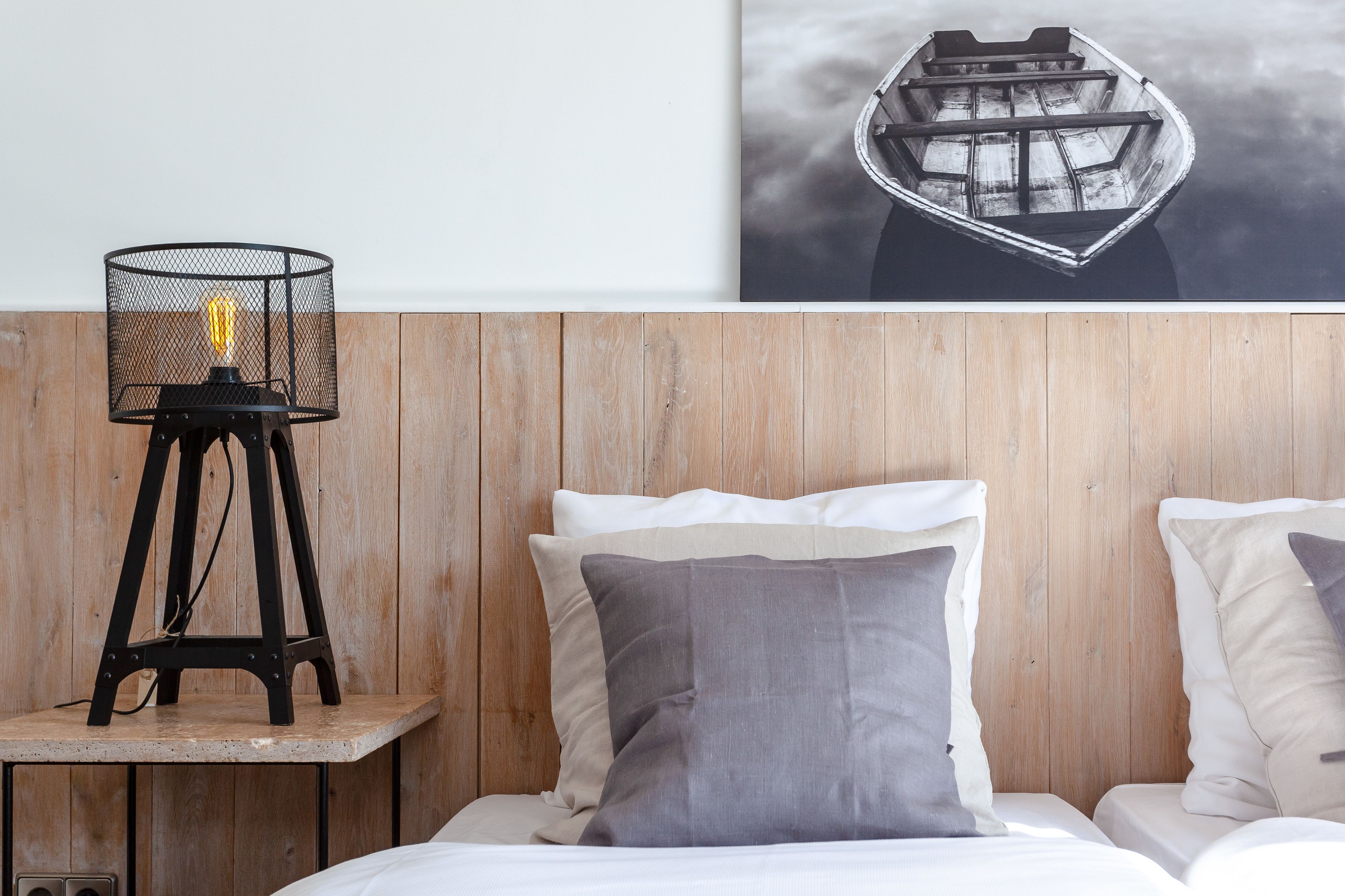 Cabecera de madera con cama, almohadas y una mesita de noche con lámpara.