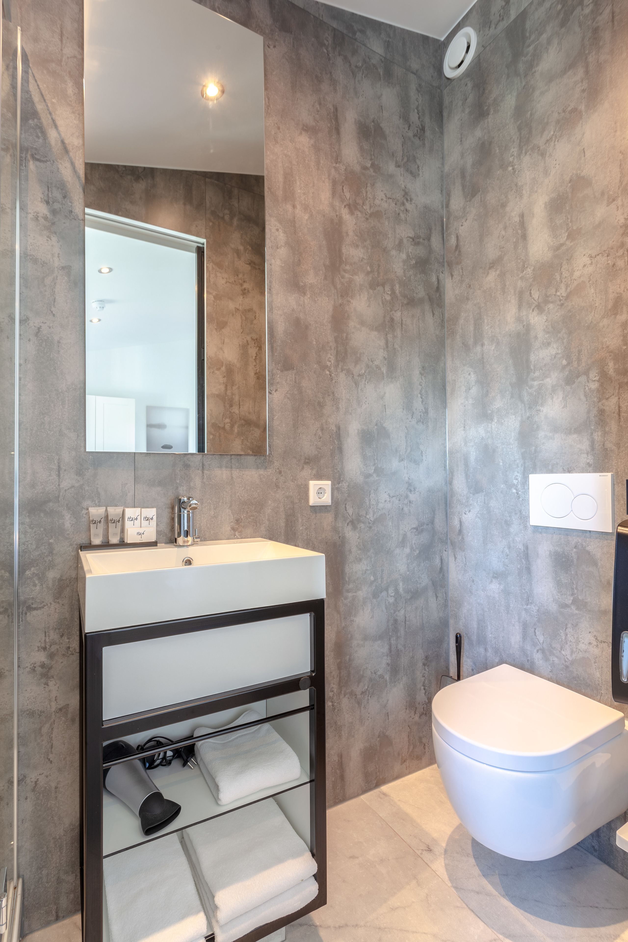 Un baño moderno con un espejo grande, un lavamanos blanco y un inodoro.