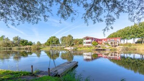 Une propriété au bord du lac, avec une jetée en bois, un bâtiment rouge doté d’un balcon et un ciel bleu azur.