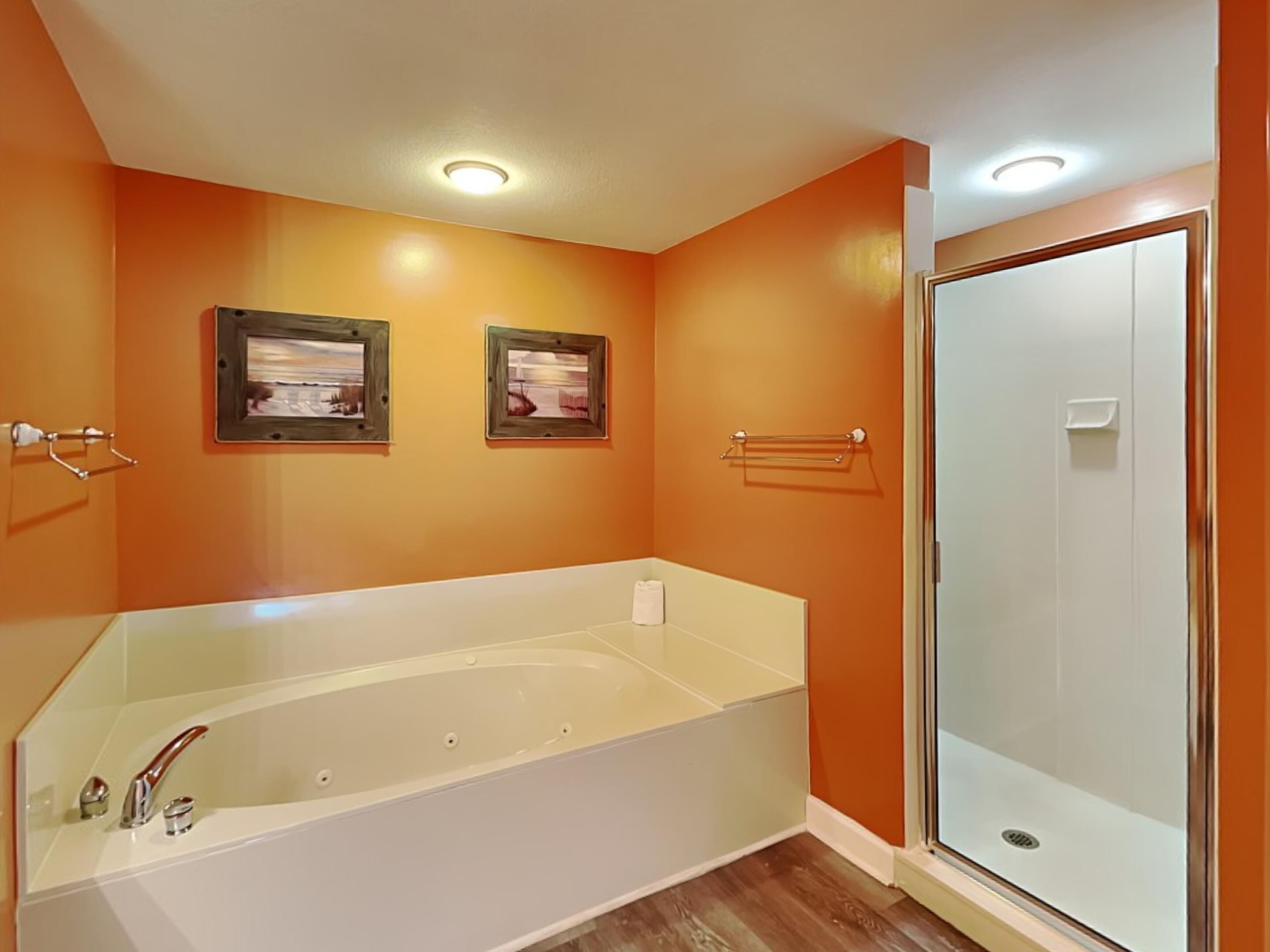 Un baño con una pared naranja, una bañera blanca y un box de ducha de vidrio.