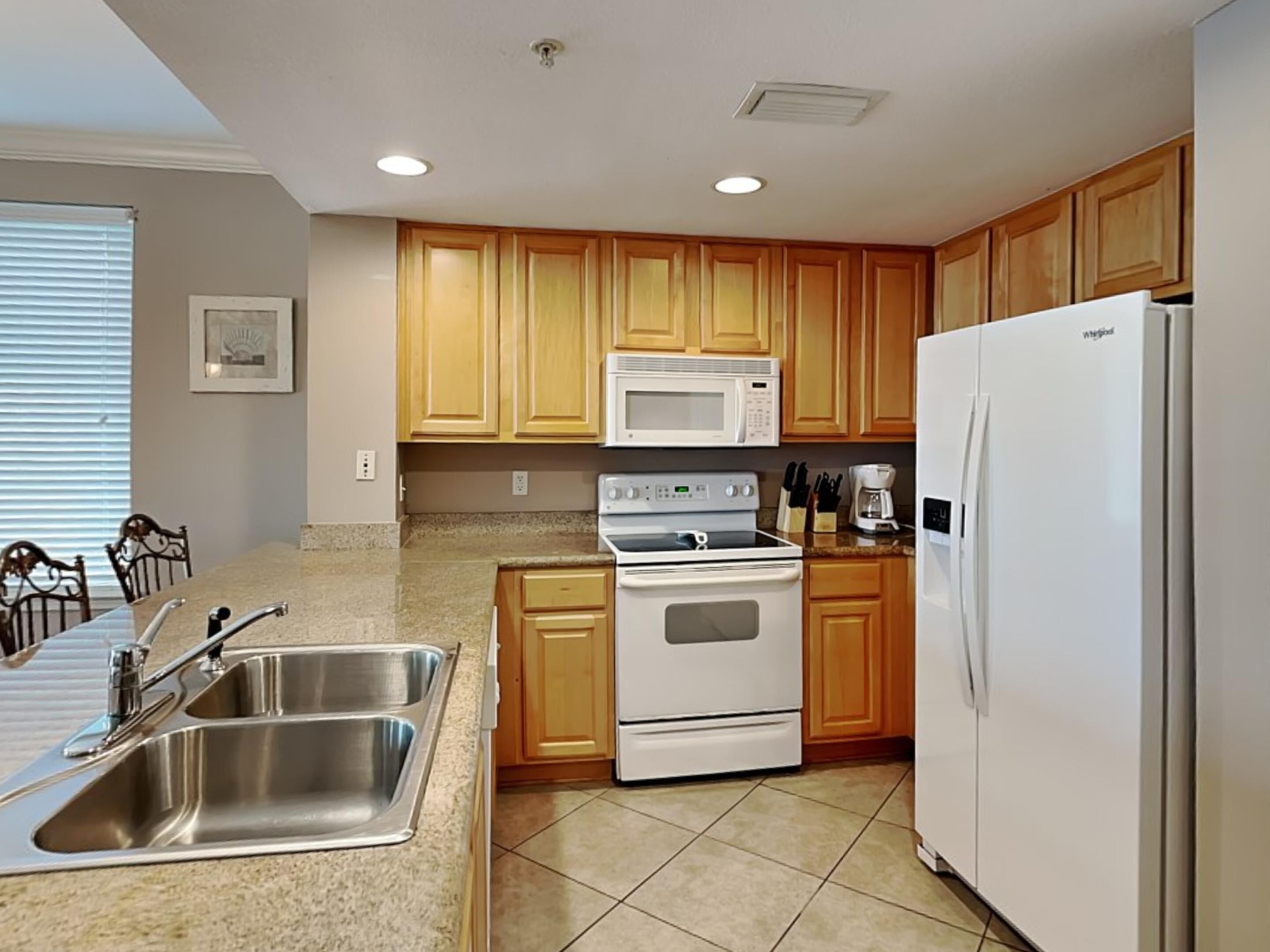 A modern kitchen with wooden cabinets, a stainless steel sink, a white refrigerator, and a built-in oven.