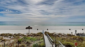 Ein Strand mit einem hölzernen Steg, der zum Wasser führt, einem Reetdachschirm und einem Schild, das einen Privatbereich kennzeichnet.