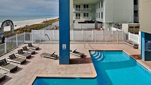 Ein Poolbereich auf dem Dach mit Liegestühlen, einem Sprungverbotsschild und Blick auf den Strand.