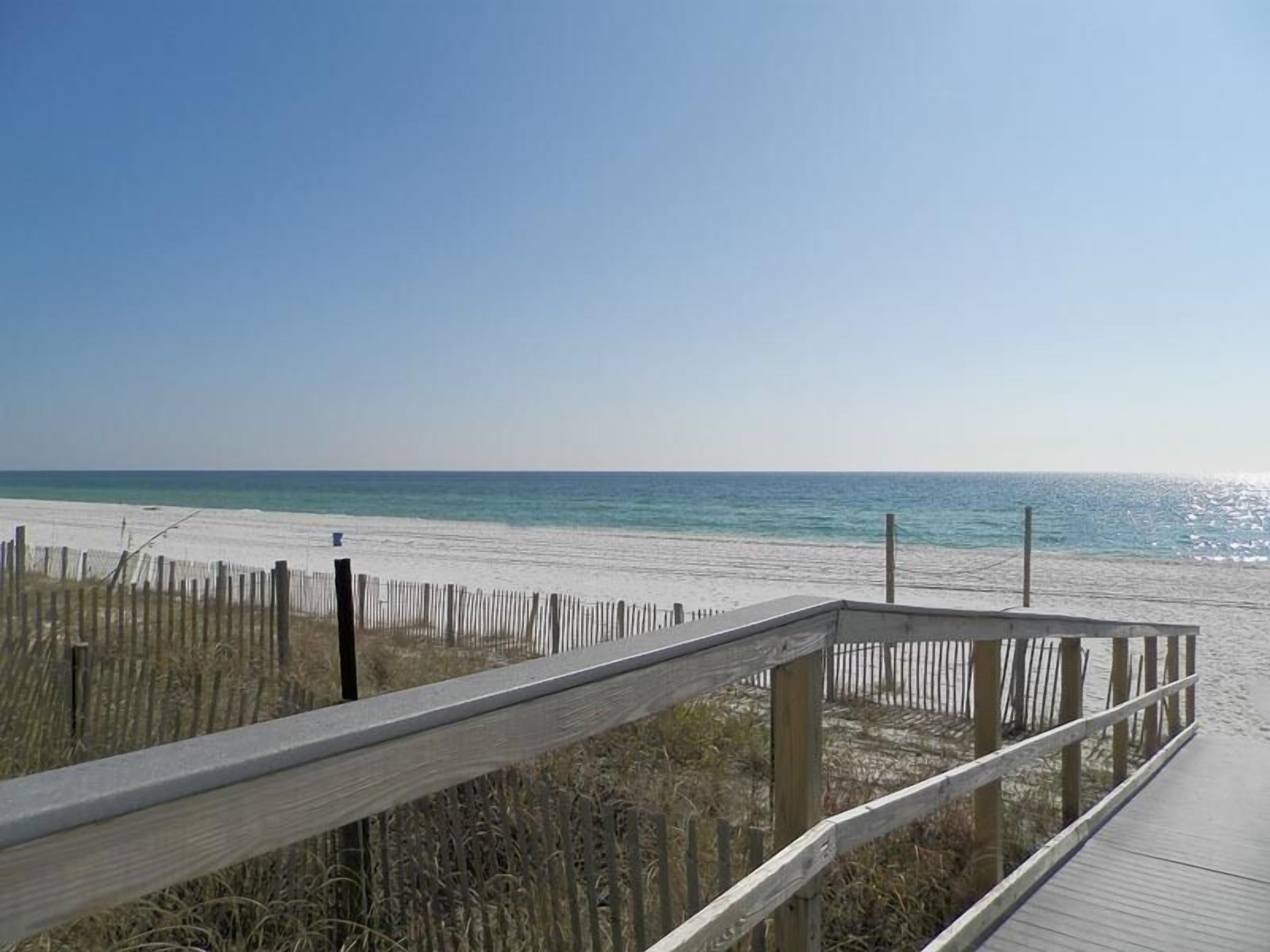 A wooden boardwalk leading to a sandy beach with a clear sky.