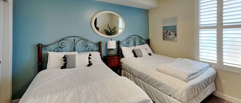 A bedroom with two beds, a ceiling fan, a round mirror, and a window with blinds.