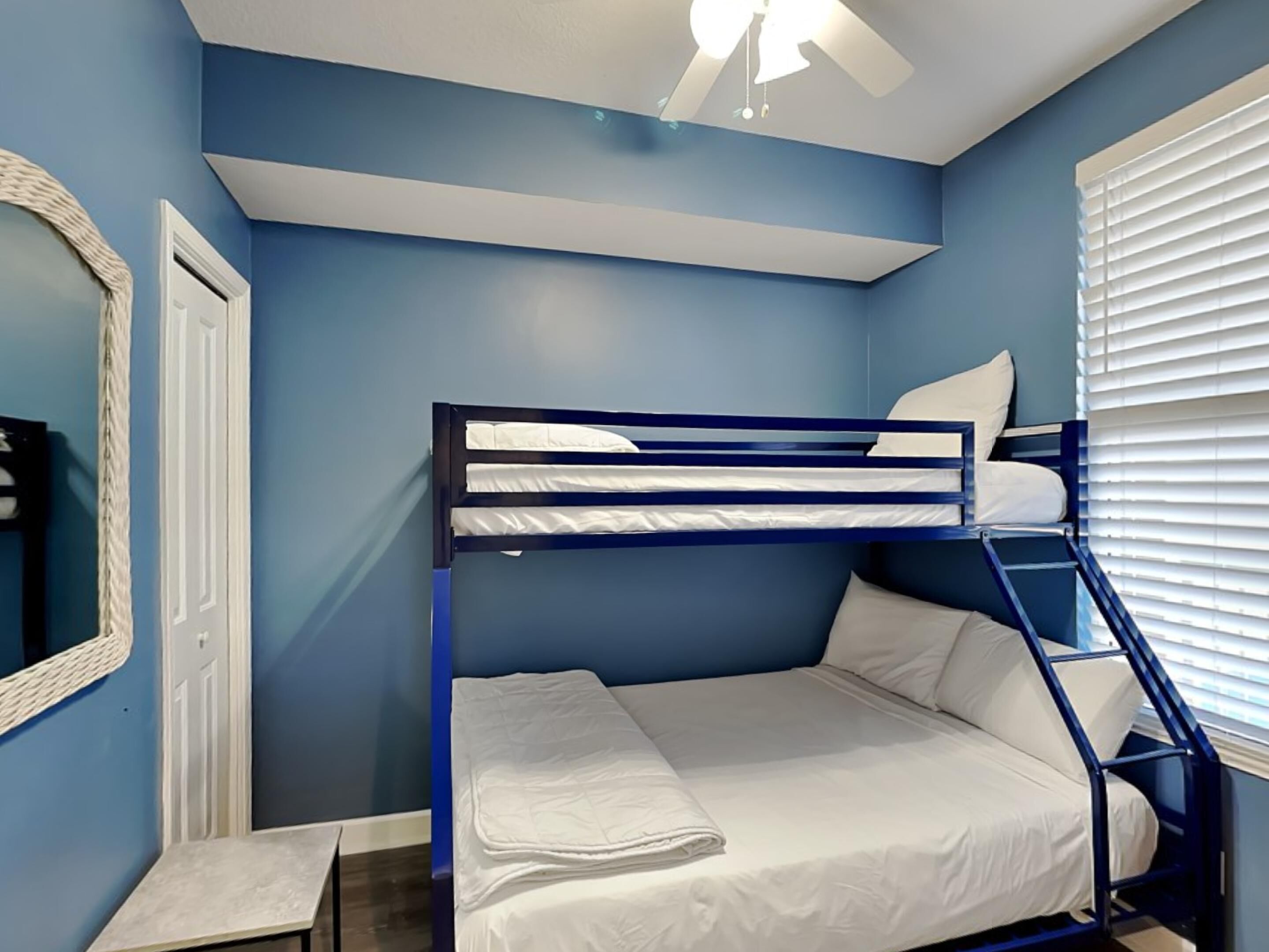 A bunk bed room with a ceiling fan, a window with blinds, and a mirror on the wall.