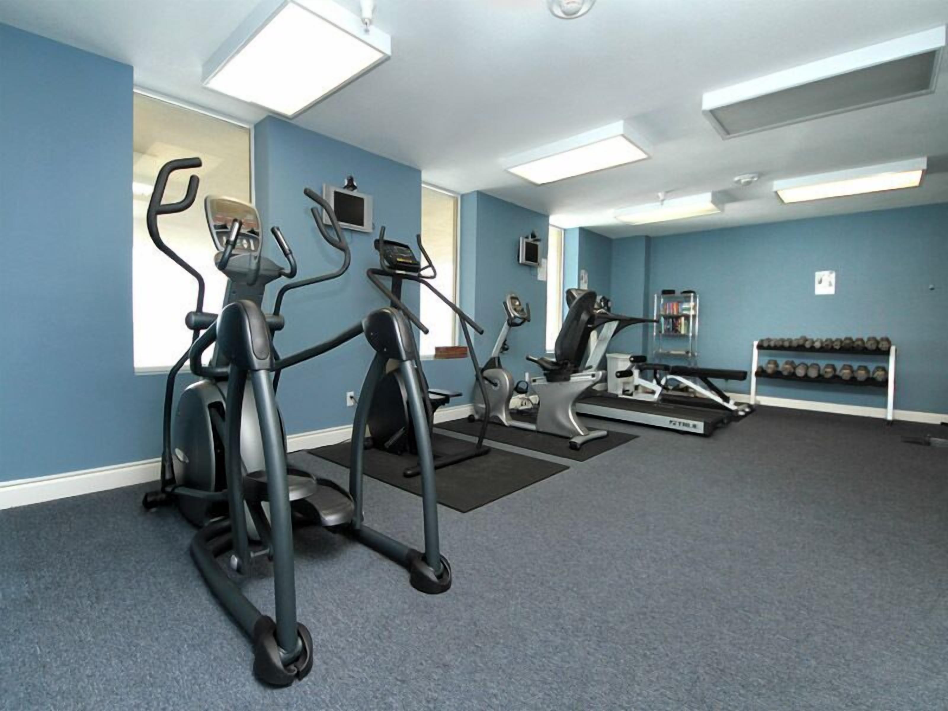 Een sportschool met loopbanden, elliptische trainers en een dumbbellsrek.