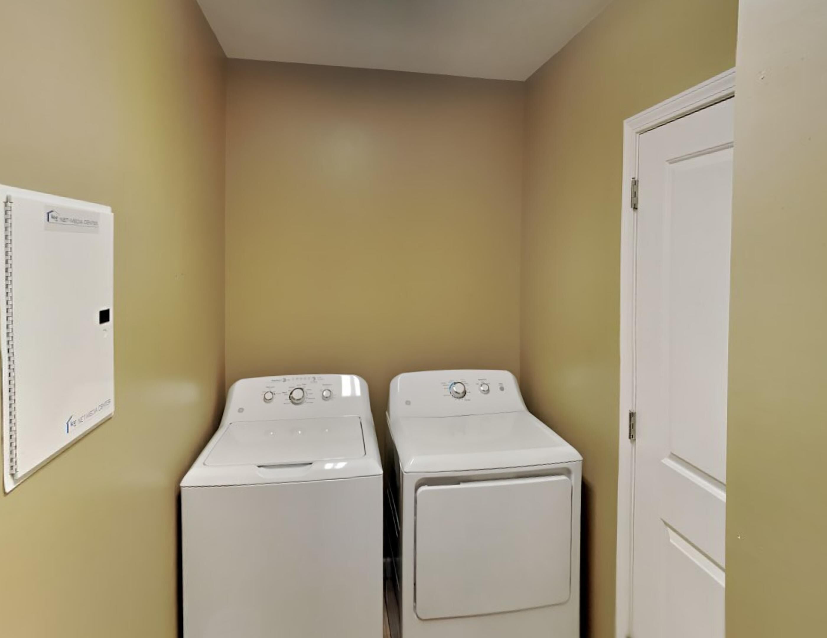 A laundry room with two white washing machines and a white utility box on the wall.