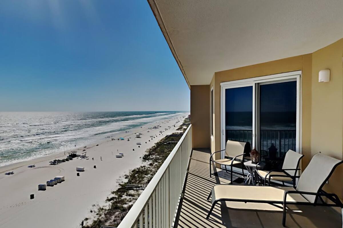 Varanda com vista para a praia, mobiliário de exterior e uma janela grande.