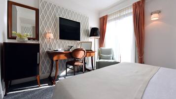 A hotel room with a bed, a desk, a chair, a TV, and a lamp.